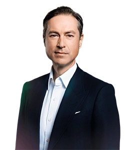 Professional portrait of a middle-aged man in a dark suit and white shirt, looking at the camera against a plain background.