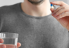 Enclomiphene Dosage and What to Expect in the First 90 Days Person in a gray sweater holds a blue-and-white capsule above a glass of water, ready to take a pill.
