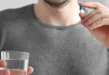 Enclomiphene Dosage and What to Expect in the First 90 Days Person in a gray sweater holds a blue-and-white capsule above a glass of water, ready to take a pill.